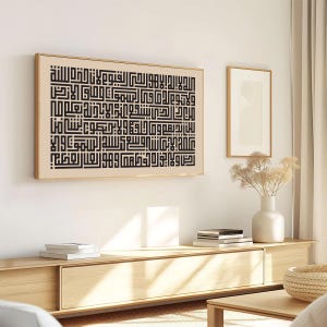 May include: A black and white Islamic calligraphy print in a wooden frame, hanging on a white wall above a wooden shelf with books and a wooden table with a woven basket.