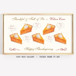 Puede incluir: Una impresión enmarcada con borde dorado presenta ilustraciones en acuarela de rebanadas de pastel de calabaza cubiertas con crema batida. El texto incluye "Thankful & Full of Pie - Wilson Crew" y "Happy Thanksgiving". La impresión es de Cozy Nest Gallery.