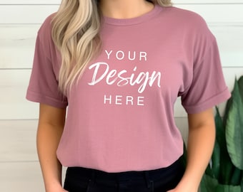 May include: Mauve-colored t-shirt with rolled sleeves. The shirt features the text "YOUR Design HERE" in a white, handwritten-style font. The model is wearing black pants.