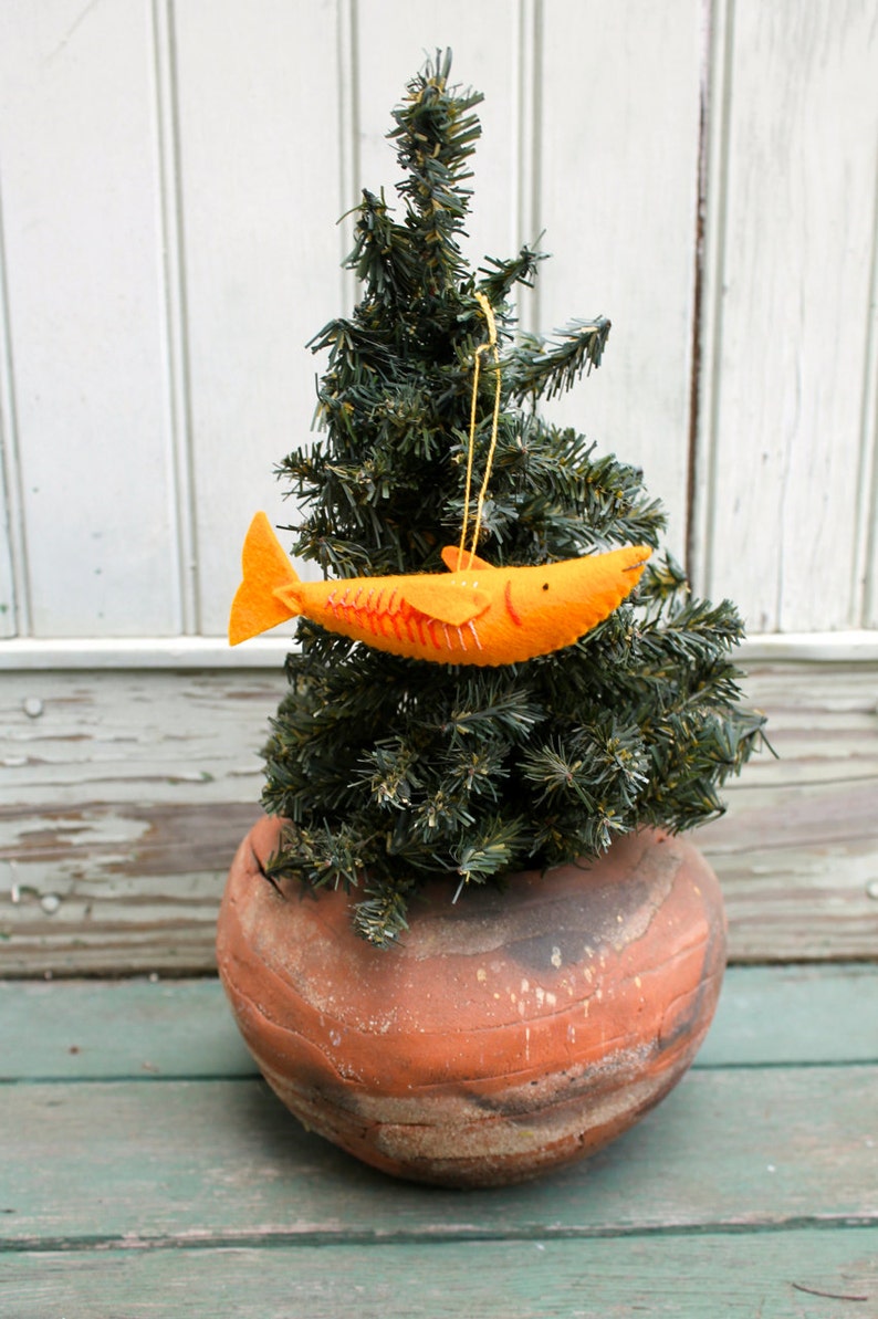 May include: A small artificial Christmas tree with a felt orange fish ornament hanging from it. The tree is in a terracotta pot.