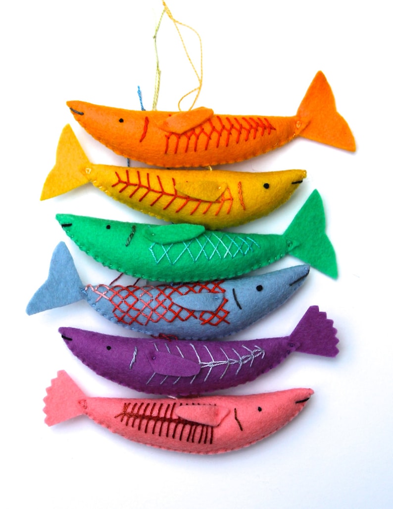 May include: A set of six felt fish ornaments in a rainbow of colors, hanging from a string. The fish are all different sizes and have embroidered details, including eyes, fins, and scales.