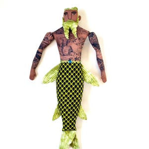 May include: A handmade mermaid doll with a tattooed torso, green beard, and a black and yellow scale-patterned tail. The doll has articulated arms and a blue gem on the waist. The mermaid's fins are green.