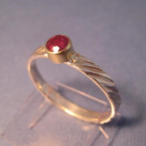 May include: A silver ring with a twisted band and a red gemstone set in a gold bezel.
