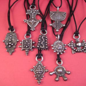 May include: Eight silver pendants with intricate designs hang from black cords. The pendants feature geometric shapes, raised dots, and a variety of textures.