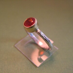 Puede incluir: Un anillo de plata con una banda texturizada y una piedra preciosa roja engastada en un engaste de oro.