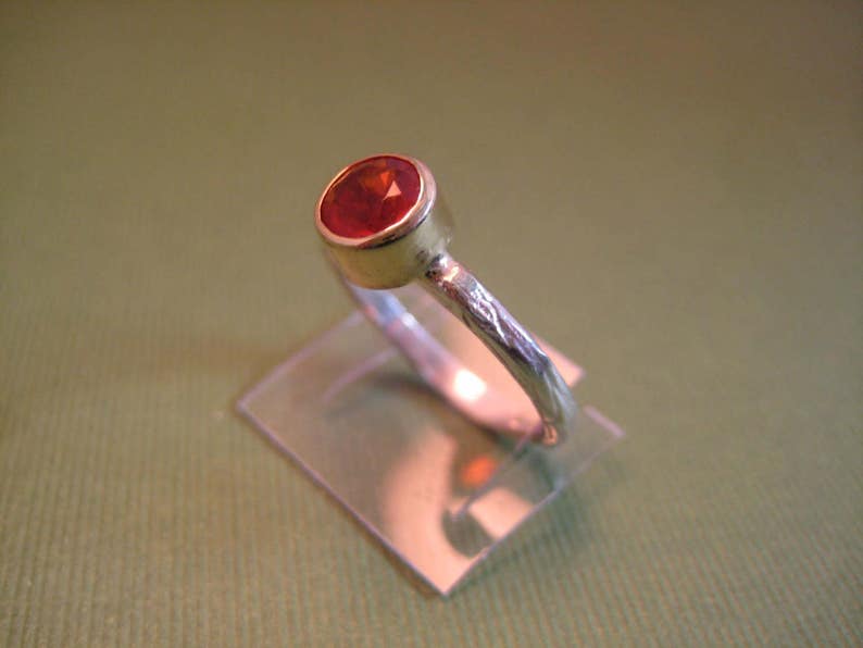 Puede incluir: Un anillo de plata con una banda texturizada y una piedra preciosa roja engastada en un engaste de oro.