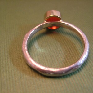 Puede incluir: Un anillo de plata con una banda texturizada y una piedra preciosa roja engastada en un engaste de oro.