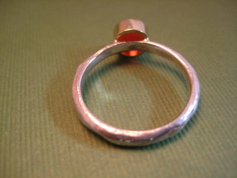 Puede incluir: Un anillo de plata con una banda texturizada y una piedra preciosa roja engastada en un engaste de oro.