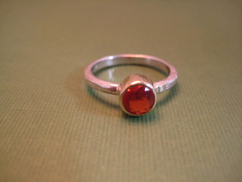 Puede incluir: Un anillo de plata con una piedra preciosa roja engastada en un engaste de bisel.