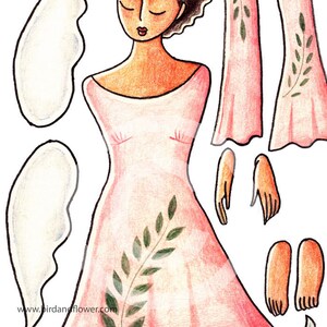 May include: A paper doll with a pink dress and green leaves. The doll has brown hair and brown eyes. The doll is wearing a pink dress with a green leaf design. The doll has separate arms, legs, and a head.