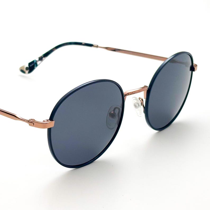 Pu&ograve; includere: Occhiali da sole rotondi blu con montatura in oro rosa. Gli occhiali hanno un design classico e senza tempo.