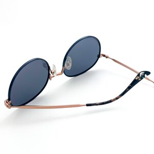 Pu&ograve; includere: Occhiali da sole rotondi in oro rosa con lenti blu scuro e aste in tartaruga.