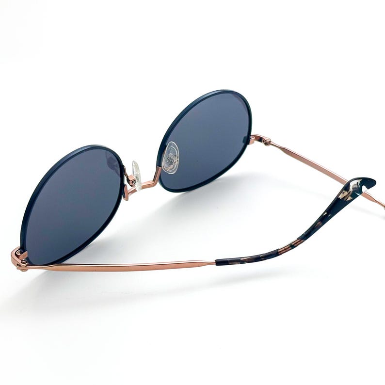 Pu&ograve; includere: Occhiali da sole rotondi in oro rosa con lenti blu scuro e aste in tartaruga.