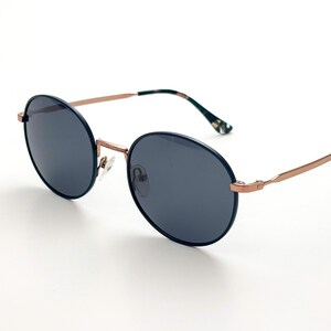 Pu&ograve; includere: Occhiali da sole rotondi di colore grigio scuro con montatura in metallo color oro rosa. Gli occhiali hanno un design classico e minimalista.