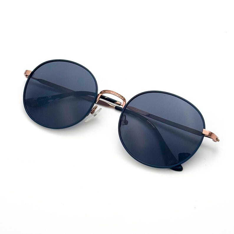 Pu&ograve; includere: Occhiali da sole rotondi con lenti blu e montatura in metallo color oro rosa.