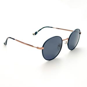 Pu&ograve; includere: Occhiali da sole rotondi, blu scuro, con montatura in metallo color oro rosa. Gli occhiali hanno un design classico e senza tempo.