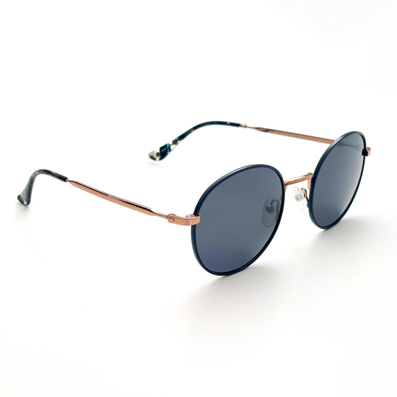 Pu&ograve; includere: Occhiali da sole rotondi, blu scuro, con montatura in metallo color oro rosa. Gli occhiali hanno un design classico e senza tempo.