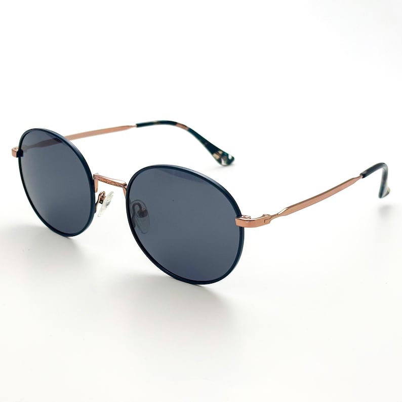Pu&ograve; includere: Occhiali da sole rotondi blu scuro con montatura in metallo color oro rosa. Gli occhiali hanno un design classico e senza tempo.