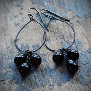 May include: A pair of black dangle earrings with three black beads hanging from each earring. The earrings are made of thin black wire and have a simple, elegant design.