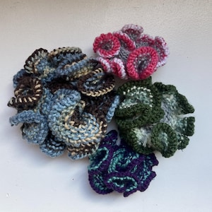 Puede incluir: Cuatro decoraciones de arrecife de coral de ganchillo en diferentes colores: azul, marrón, verde y rosa. El coral está hecho con una variedad de puntadas y texturas.