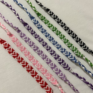 Könnte beinhalten: Ein Set aus acht Freundschaftsarmbändern mit Chevron-Mustern in verschiedenen Farben, darunter Rot, Rosa, Lila, Blau, Grün und Schwarz.