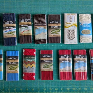 May include: A collection of fifteen packaged sewing notions including Wrights bias tape, quilt binding, and rick rack in various colors such as blue, brown, red, and white. Each package features printed labels with brand names and product details.