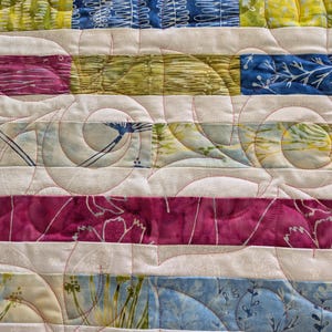 May include: A quilt featuring horizontal strips of fabric in shades of blue, green, and magenta, interspersed with off-white fabric strips. The entire surface is covered in continuous, swirling, curved machine quilting stitches in red thread.