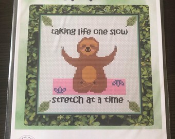 May include: Cross stitch pattern featuring a sloth in a yoga pose with the text "taking life one slow stretch at a time".