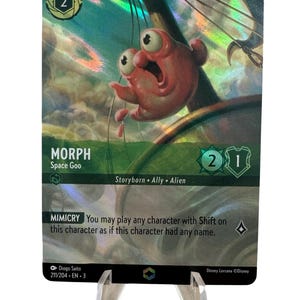 May include: A holographic trading card featuring the character Morph from Space Goo. The card has a pink alien illustration with large eyes and the number 2 in a green circle. The card is displayed on a clear stand.
