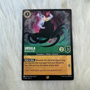 May include: A trading card featuring Ursula, the sea witch from Disney's The Little Mermaid. The card is black with gold accents and features an illustration of Ursula with her tentacles. The card text reads "Ursula, Deceiver of All. Dreamborn. Villain. Sorcerer. What a Deal: Whenever this character sings a song, you may play that song again from your discard for free, then put it on the bottom of your deck. "I don't want much-just the most powerful lore!" "