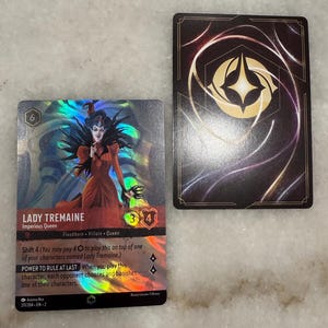 May include: A collectible card game card featuring Lady Tremaine, a villain from the Disney movie Cinderella. The card is holographic and features a purple, blue, and green iridescent background. The card text reads "Shift 4 (You may pay 40 to play this on top of one of your characters named Lady Tremaine.) Power to Rule at Last When you play this character, each opponent chooses and banishes one of their characters."