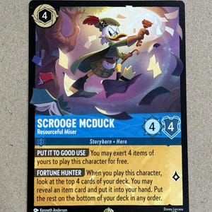 May include: Scrooge McDuck trading card from the Disney Lorcana game. The card features a colorful illustration of Scrooge McDuck in his signature outfit, holding a bag of money and a walking stick. The card text reads "Scrooge McDuck, Resourceful Miser, Storyborn - Hero, Put it to Good Use: You may exert 4 items of yours to play this character for free. Fortune Hunter: When you play this character, look at the top 4 cards of your deck. You may reveal an item card and put it into your hand. Put the rest on the bottom of your deck in any order."