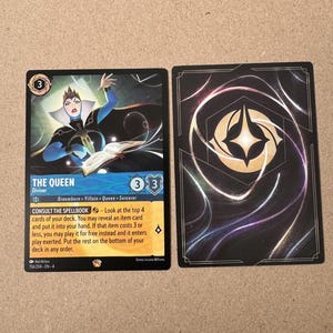May include: A trading card game card featuring the Evil Queen from Snow White. The card is blue and gold with an illustration of the Evil Queen holding a book. The card text reads "The Queen" and "Consult the Spellbook - Look at the top 4 cards of your deck. You may reveal an item card and put it into your hand. If that item costs 3 or less, you may play it for free instead and it enters play exerted. Put the rest on the bottom of your deck in any order."