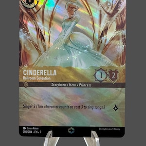 May include: A collectible trading card featuring Cinderella in a shimmering gown. The card has a holographic effect and includes the text "CINDERELLA Ballroom Sensation". It is supported by a clear acrylic stand.