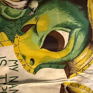 May include: A white fabric panel featuring a green and yellow illustration of a creature with large dark eyes. The text printed in green reads MY NAME IS TIPE THE T. The design includes yellow scalloped borders and dark brown accents on the creature.