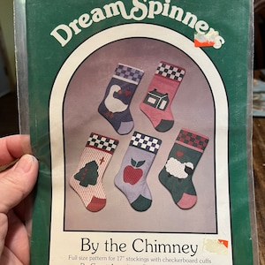 Könnte beinhalten: Eine Packung mit einem Quiltmuster namens "Dream Spinners" mit fünf Weihnachtsstrumpf-Designs. Jeder Strumpf hat ein anderes Design, darunter eine Gans, ein Haus, ein Apfel, ein Baum und ein Schaf. Das Muster ist für 43 cm Strümpfe.