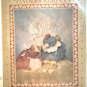 May include: A Craft Patch pattern titled "Finders Keepers" featuring two stuffed fabric chickens. One is red and the other is blue, both with white accents. The background has a neutral color palette with a heart-shaped border.
