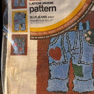 May include: A Caron latch hook pattern kit titled Bluejeans #3017, featuring a 100% cotton canvas with a finished size of 20 inches by 27 inches. The packaging displays three color variations of a blue jeans design with patches and hearts.