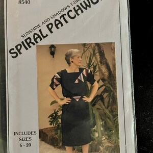 May include: A sewing pattern package for a "Sunshine and Shadows T-Dress" by Spiral Patchwork. The package features a photo of a woman wearing a black dress with geometric accents in pink, white, and blue. Sizes 6-20 are included.
