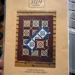 Puede incluir: Un paquete que presenta un patrón de edredón con un diseño Double Paw Block, adecuado para un camino de mesa y un edredón de pared. El diseño del edredón incluye cuadrados con patrones de estrellas en tonos de azul, blanco y burdeos. El paquete está etiquetado como "MH Designs".