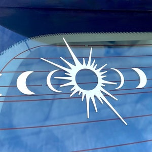May include: White vinyl sticker with a sun and moon phases design. The sun is stylized with rays and the moon phases are in a crescent shape.