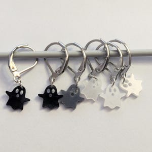 May include: Six ghost-shaped charms in black, grey, and white, each suspended from a silver leverback clasp. The charms are arranged on a grey knitting needle. Ideal for Halloween-themed crafts, these charms add a spooky touch.