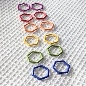 May include: A set of ten colourful hexagonal rings in a rainbow pattern. The rings are made of metal and are arranged in a row from purple to blue.