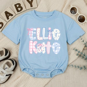 May include: A light blue short-sleeved baby bodysuit featuring the name Ellie Kate printed in large, decorative letters. The letters are filled with various patterns including pink and blue gingham, blue floral prints, and stripes, accented with small pink bows.
