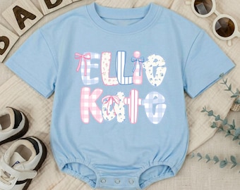 Puede incluir: Un body de bebé de manga corta en color azul claro con el nombre Ellie Kate impreso en letras grandes y decorativas. Las letras tienen varios patrones, incluyendo cuadros vichy rosas y azules, estampados florales azules y rayas, con lazos rosas.