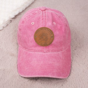 May include: Pink baseball cap with a brown leather patch that says "Dream, Explore, Discover" with a rainbow and clouds and the name "Elysia" underneath.