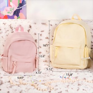 May include: Two canvas backpacks, one pink and one yellow, with drawstring closures and a zippered pocket. The pink backpack measures 9.45 inches wide, 12.6 inches tall, and 4.72 inches deep. The yellow backpack measures 11.8 inches wide, 16.1 inches tall, and 5.12 inches deep.