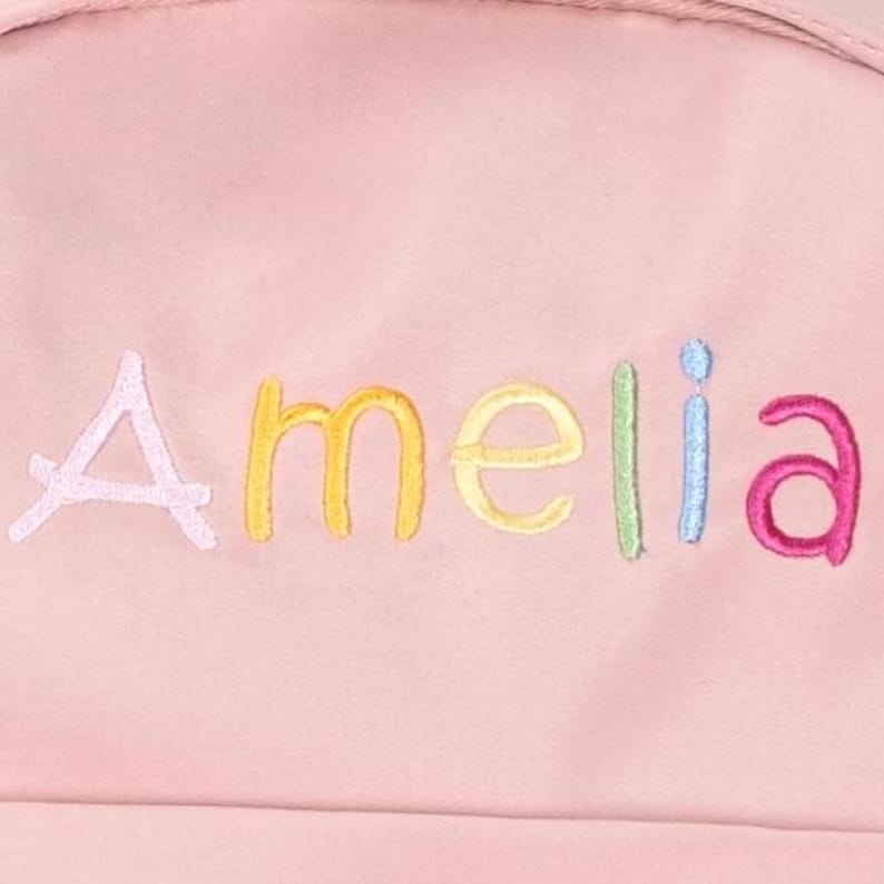 May include: Pink backpack with the name Amelia embroidered in rainbow colors.