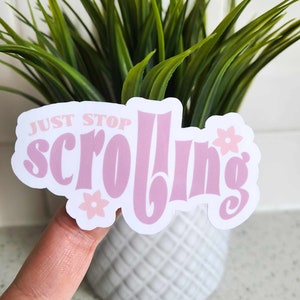 May include: Pink and white sticker with the text "JUST STOP SCROLLING" in a retro font. The sticker has two small pink flowers on it.