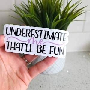 May include: White sticker with black text that reads "UNDERESTIMATE me THAT'LL BE FUN". The word "me" is written in purple.